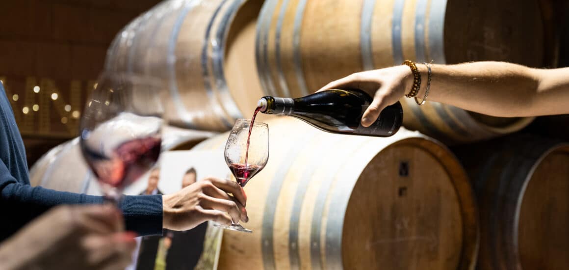 Main tendant une bouteille pour servir un verre de vin dans une cave